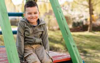 Lächelnder Junge sitzt auf Spielgerüst